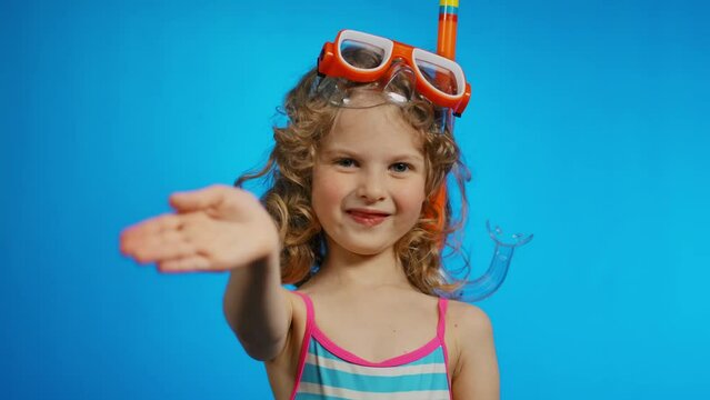 A cute curly girl with a diving mask smiling and wavingin in the studio on the blue background