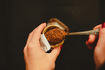 The woman takes out a portion of instant coffee from a jar with a teaspoon. An invigorating drink...