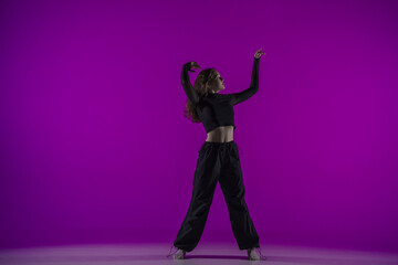 Energetic contemporary dance in purple studio light: young girl in black clothes shows grace and...