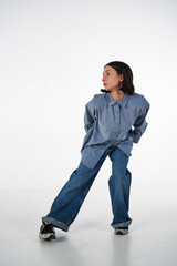 A young woman in denim casual wear poses in a studio against a white background. The dancer...