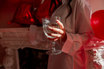 Close-up of womans hand with glass of champagne with festive manicure with red hearts on the nail, silver ring. Celebrating Valentines Day, Engagement, Birthday. Jewelry for hand. Creative holiday