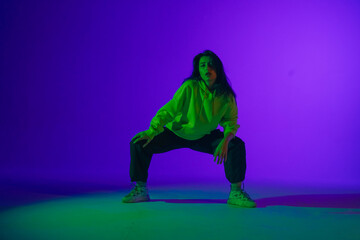 Fototapeta na wymiar Live jazz-funk performance in the studio: a young stylish girl in casual clothes embodies the rhythm and energy of dance under purple-green light.