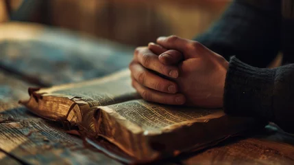 Photo sur Plexiglas Vielles portes Person's hands folded in prayer over an open, well-worn bible, resting on a wooden table