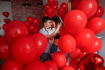 In middle of room with many red heart balloons stands tender couple in love. Creative home...