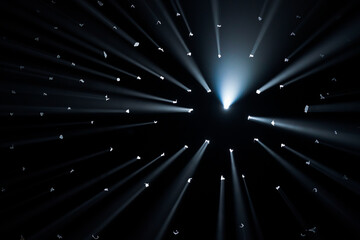 Rays of bright light come through holes in the black background of the studio. The rays cut through...