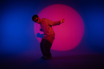 Guy in casual clothes dancing hip hop elements in studio with blue light. Dancer is in red circle of spotlight and demonstrates body plasticity. Full height. Modern street choreography.