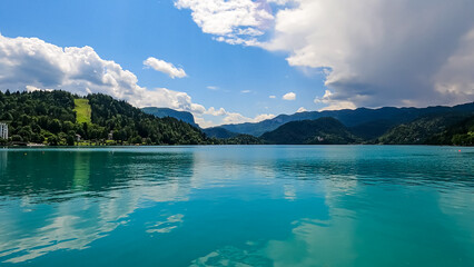 Panoramic view of St Mary Church of Assumption build on small island on alpine lake Bled, Upper Carniola, Slovenia. Serene landscape in Julian Alps in summer. Hills covered with lush green forest - obrazy, fototapety, plakaty