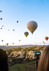 Hot air balloon flying over Cappadocia Turkey in the morning. A woman recording the scene with her...