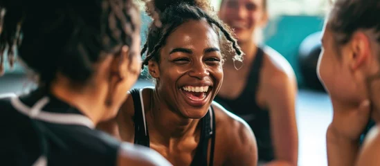 Rolgordijnen Fitness Young woman laughing with diverse friends on a gym floor after exercise.