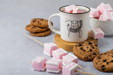 Cup with a fun design with cocoa and white and pink marshmallows and Americano cookies. Horizontal, space for copying.