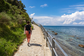 Tourist woman on scenic walking path between Fiesa and charming coastal town of Piran in Slovenian Istria, Slovenia, Europe. Rugged rocky cliffs perched above shimmering waters of the Adriatic Sea