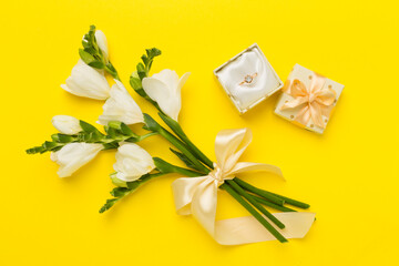 White freesia flower and gift box with diamond ring on color background, top view