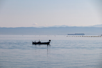 Obraz premium Fishing boat with panoramic view of idyllic coastline seen from Gulf of Piran, Adriatic Mediterranean Sea, Slovenia, Europe. Summer seaside vacation. Distant mountain ranges of Julian Alps