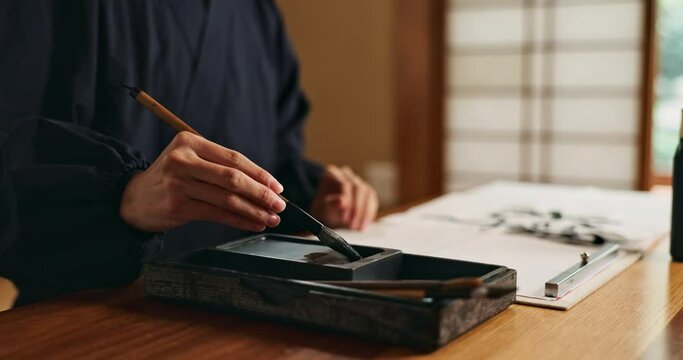 Hands, brush in ink for writing and Asian calligraphy or ancient script for art and inkstone. Japanese creativity, black paint and vintage tools, paintbrush and person with traditional stationery