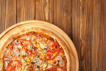 delicious pizza with chicken, mushrooms, cheese, tomatoes and corn on a wooden background
