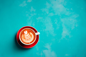 A striking red cup holding a latte with creamy art, set against a bold turquoise textured backdrop. Top view with space for text. - 702992067