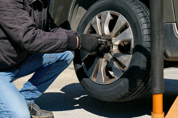 Mechanic hands in gloves changing tyre of car in garage of small repair shop.