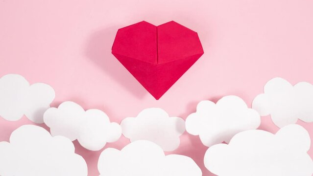 4k Volumetric origami heart swaying flies between white clouds. Greeting card. Pink background. Symbol of love. Concept of valentine's holiday, wedding and other occasions. Loop stop motion animation.