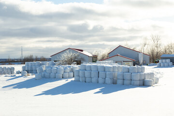 Red and white farm buildings and stacks of hay bale rolls wrapped in plastic seen during a sunny...