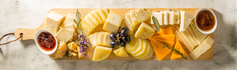 Cheese plate. Different types of cheese on a long wooden board. Horizontal banner - 702999411