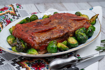 Vegan pork belly roast made with seitan and starch, served on oval plate along with roasted Brussels sprouts. Wooden table, stylish setting