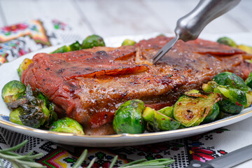 Vegan pork belly roast made with seitan and starch, served on oval plate along with roasted Brussels sprouts. Wooden table, stylish setting