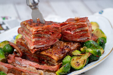 Vegan pork belly roast made with seitan and starch, served on oval plate along with roasted Brussels sprouts. Wooden table, stylish setting