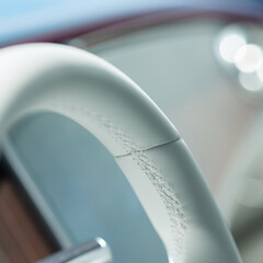 Detail of white the steering wheel. Visible seams and threads. White luxurious interior. Blur effect.