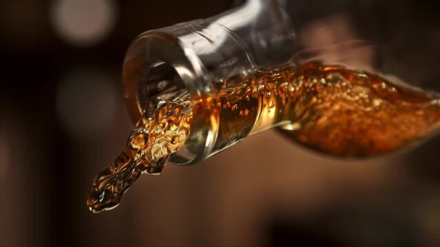 Stream of Golden Whiskey Pouring from a Transparent Bottle on a Warm Brown Wood Shade Background in Slow Motion