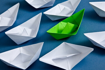 White paper boats with one green on blue background from above