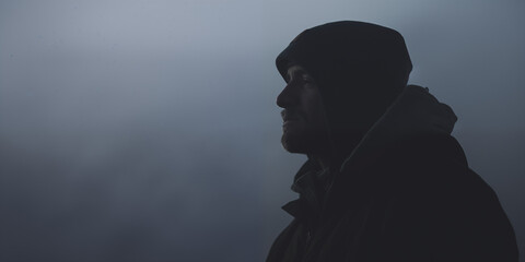 Silhouetted man against a moody, misty background, a hint of light on his contemplative face