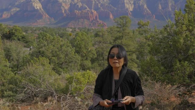 This video shows a senior asian woman taking cell phone photos of a nature mountain scene.
