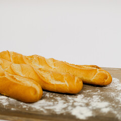 Barras de pan baguette sobre mesa de madera con harina y fondo blanco 