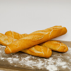 Barras de pan baguette sobre mesa de madera con harina y fondo blanco 