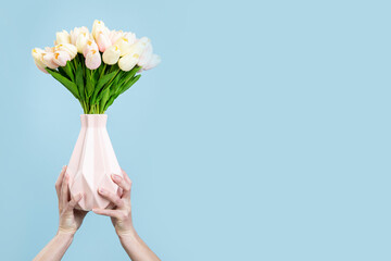 Female hands holding a vase with a bouquet of tulips on a blue background