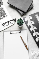 Clipboard with movie clapper, plant, eyeglasses and laptop on white background