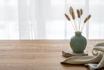 Wooden oak table top with a green vase with dry flowers and napkin. - obrazy, fototapety, plakaty