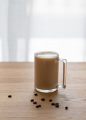 A cup of coffee with milk on a wooden table with coffee beans against the background of a window.