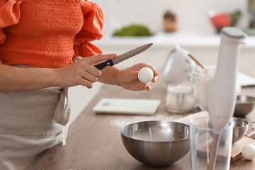 Young woman breaking egg for dough in kitchen, closeup