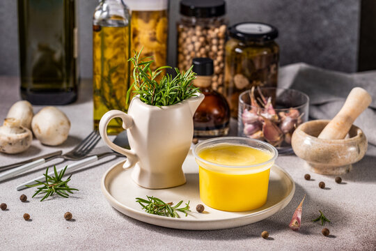 Melted butter in jar surrounded by ingredients for cooking and herbs