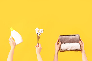 People with laundry detergent, cotton flowers and clean towels on yellow background