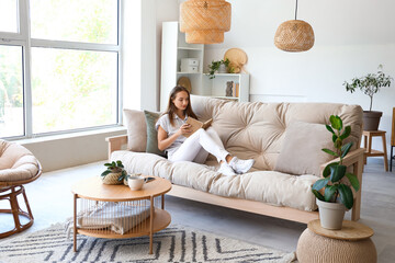 Young woman reading book on couch in living room