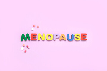 Word MENOPAUSE with pills on pink background