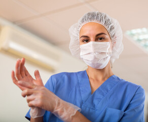 Nurse pulls gloves on her hands before the procedure, standing in the treatment room of the clinic