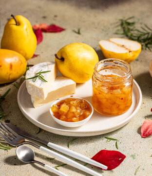 Pear jam in jar surrounded by ingredients, cheese and herbs