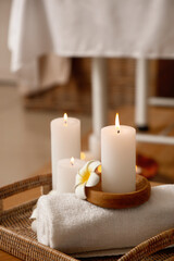 Fototapeta na wymiar Burning candles with flowers and towel on table in spa salon, closeup
