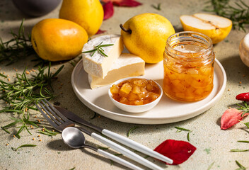 Pear jam in jar surrounded by ingredients, cheese and herbs