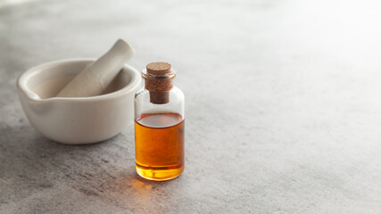 A round glass bottle containing dark orange color essential oil for cosmetics and natural medicine with white ceramic mortar and pestle.