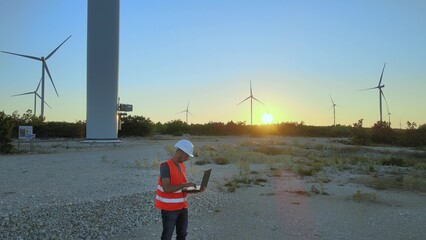 Mechanical engineer adjusting wind turbine settings from his laptop at sunset