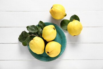 Plate with sweet ripe quinces and leaves on white wooden background